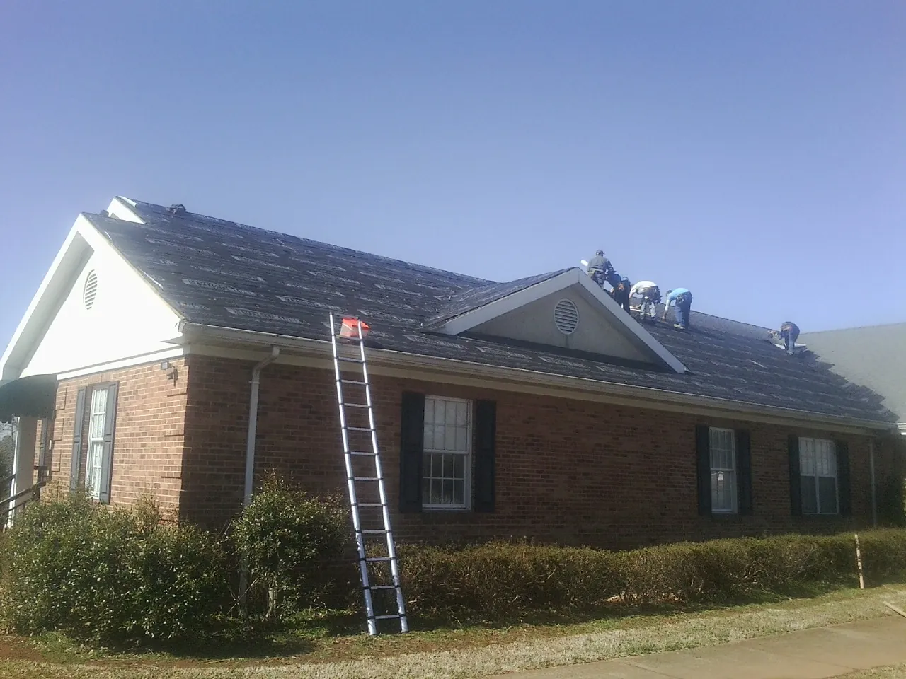 Crew tearing shingles off a brick ranch roof with a ladder set — Emergency Roof Repair work by our crew in Mount Crawford