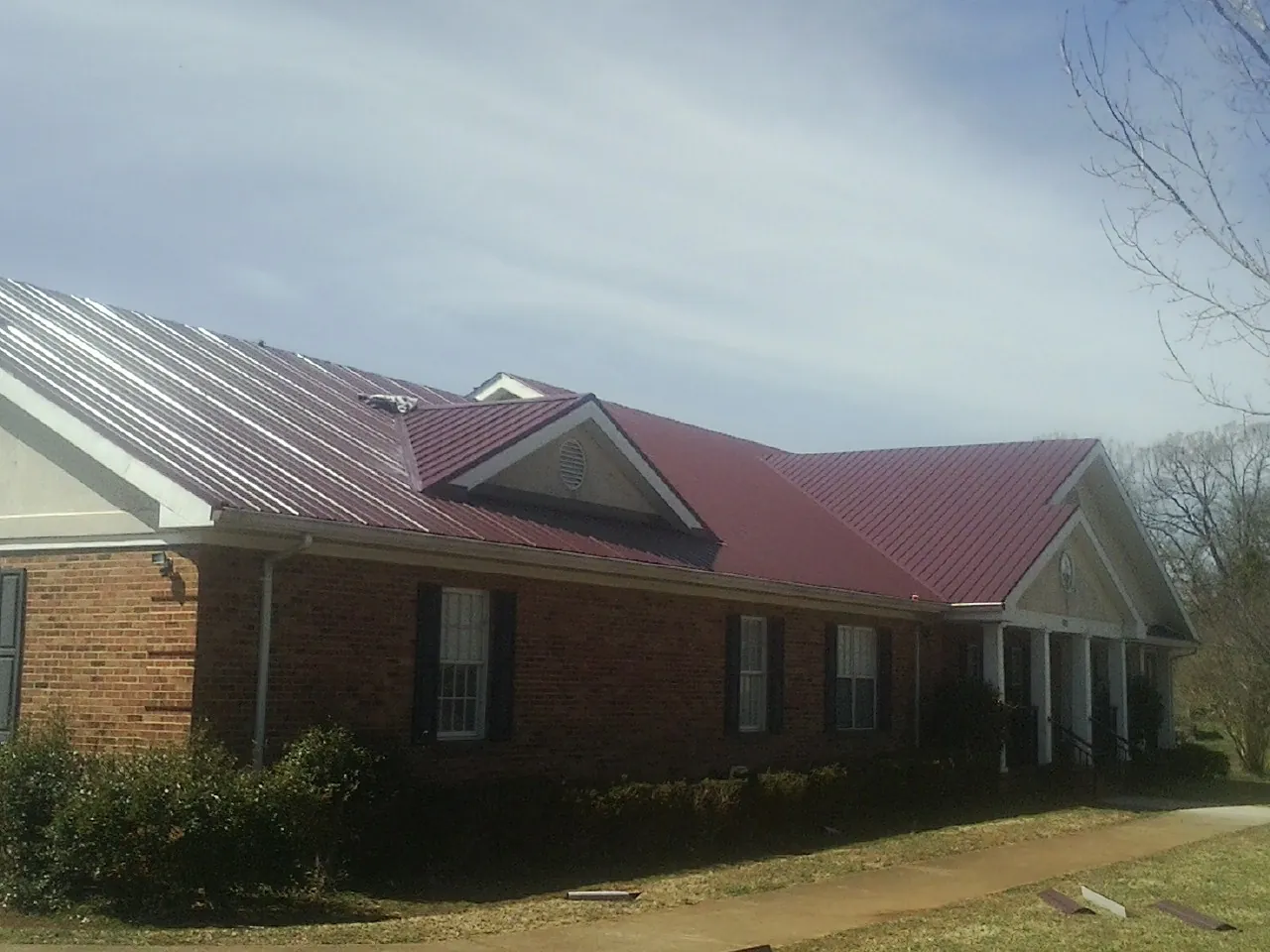 Red metal roof with gabled entries on a long brick building, from a Hail Damage Roof Repair job in Mount Crawford