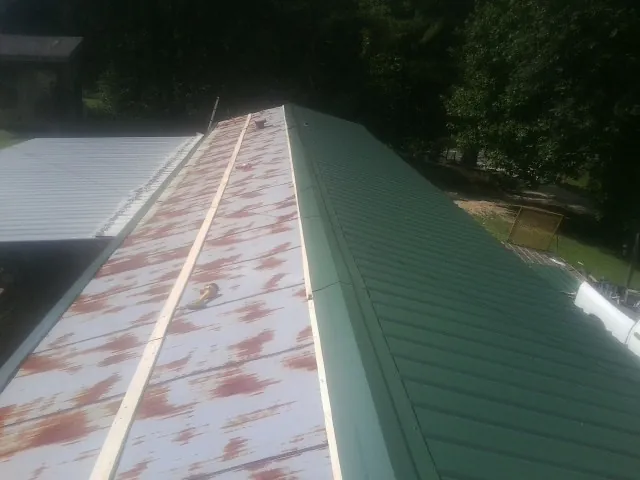 Old rusted panels beside newly installed green metal roofing — Wind Damage Roof Repair by Roofing Brothers in Mount Crawford