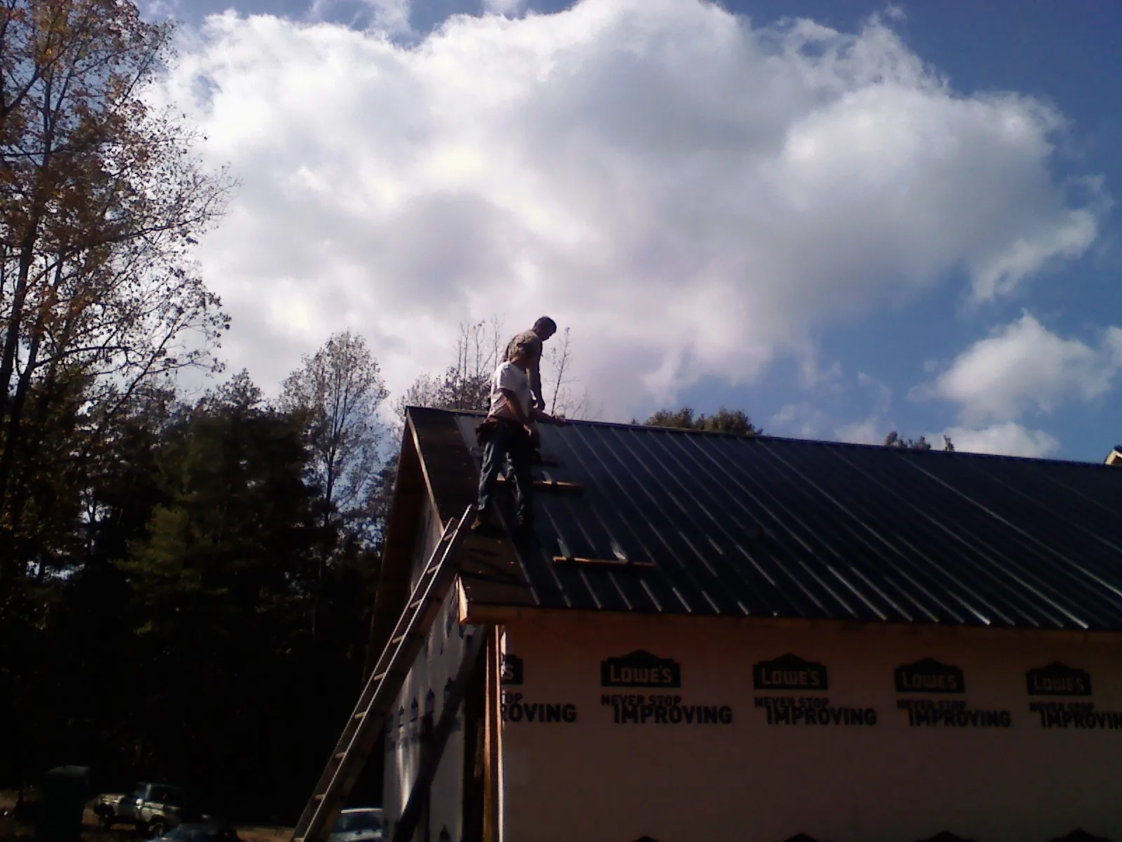 Roofer fastening dark metal panels high against a cloudy sky, from a Roof Inspection job in Mount Crawford